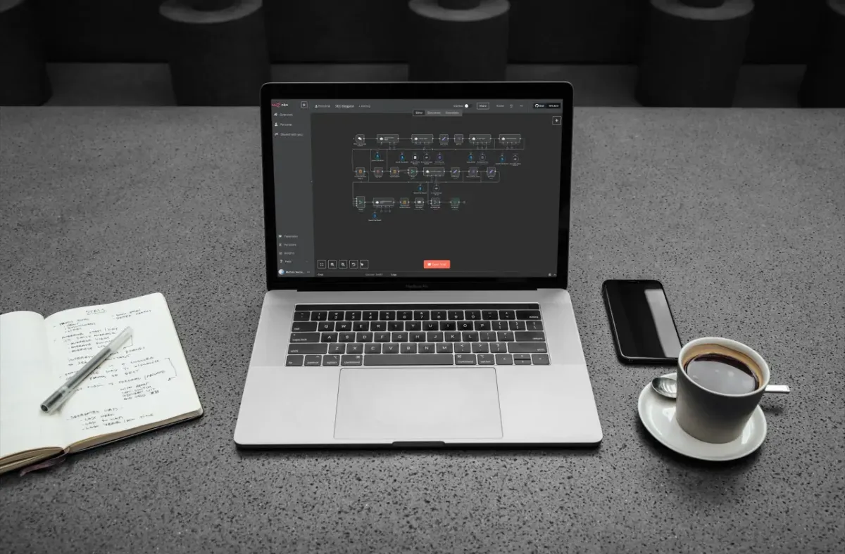 Laptop mit einem n8n-Workflow zur Podcast-Automatisierung, daneben Notizbuch und Kaffee