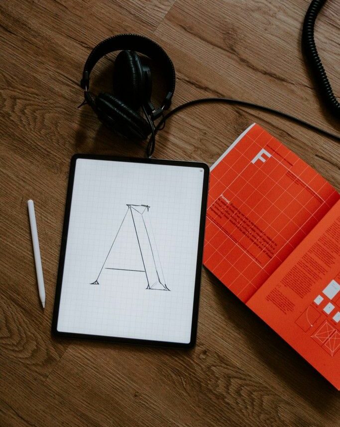 Tablet mit einem gezeichneten Buchstaben A neben Kopfhörern und einem Typografie-Buch