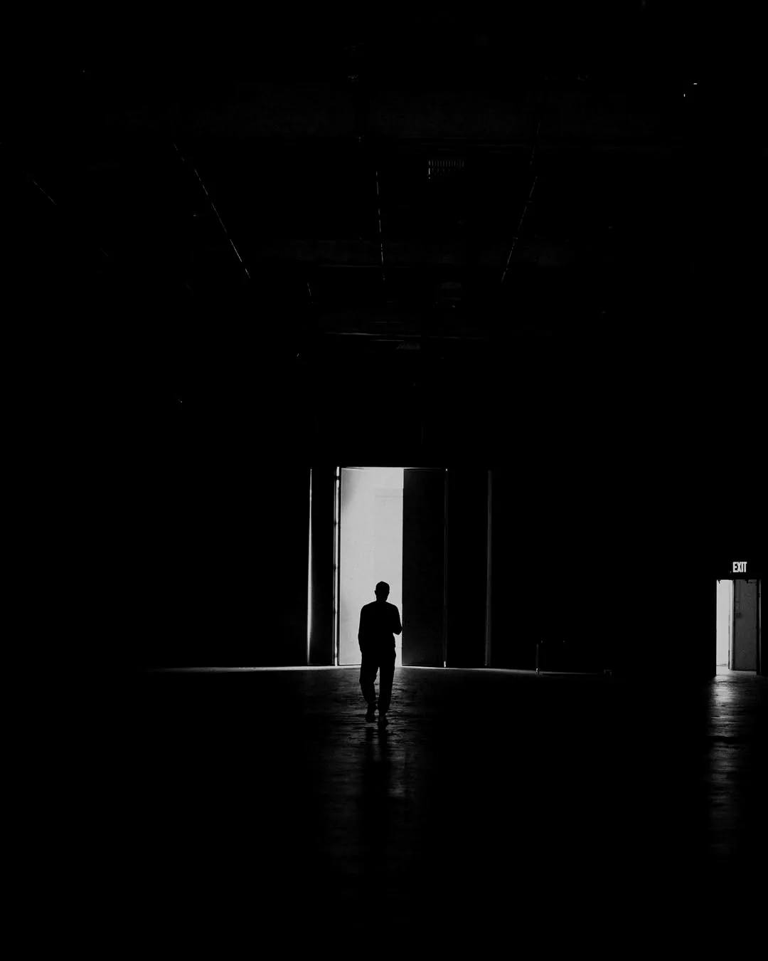 Podcast Agentur - Studio M 83 Silhouette geht in einer dunklen Halle durch eine offene, hell erleuchtete Tür