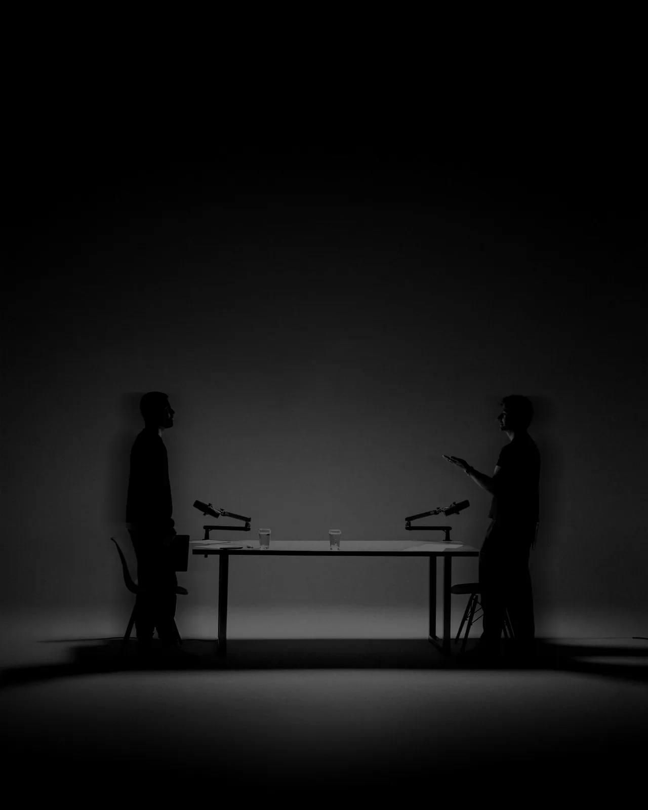 Podcast Agentur - Studio M 35 Zwei Menschen stehen sich an einem Podcast-Tisch mit Mikrofonen gegenüber, im Gegenlicht