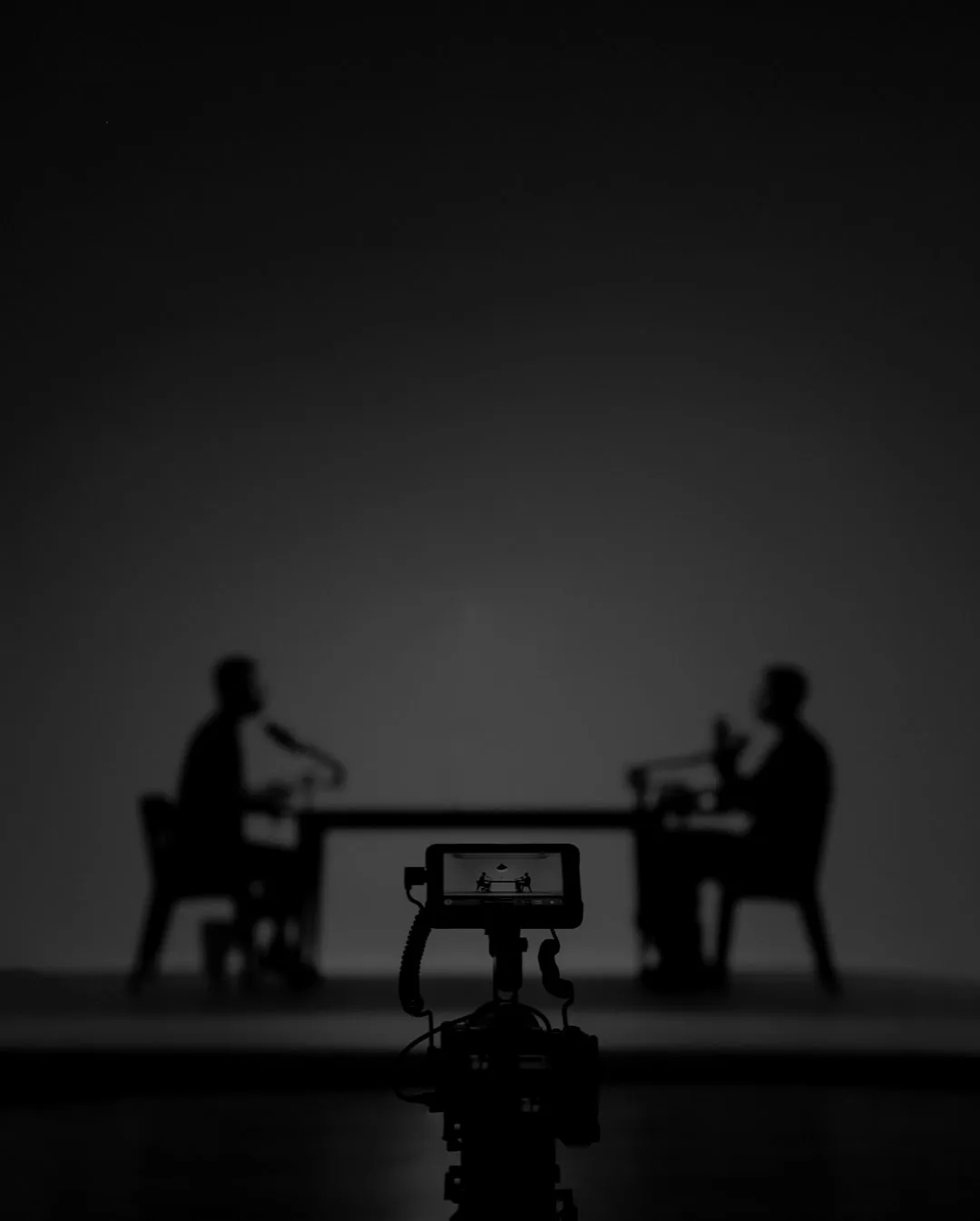 Kamera mit Monitor im Vordergrund, dahinter zwei Menschen im Podcast-Gespräch